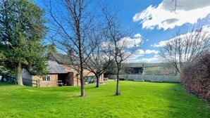 A grassy yard with a brick building, a wooden fence, and a clear blue sky. - Riverside Cottage (Marlborough)