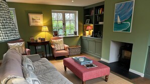A cozy living room with a sofa, armchair, and ottoman, a fireplace, and a bookshelf with books and decorative items. - Riverside Cottage (Marlborough)