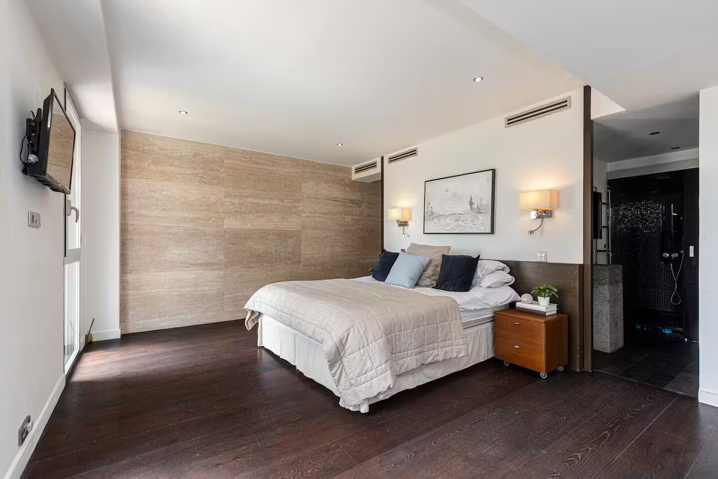 A modern bedroom with a large bed, a nightstand, a wall-mounted light, and a framed picture.