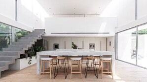 A modern kitchen with a large island, bar stools, and a staircase leading to an upper level. - Modern Villa Biot, Entire home in Biot, France (Biot)