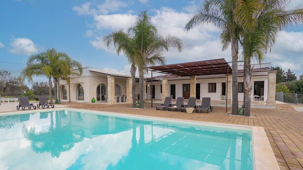 A swimming pool with lounge chairs, a covered patio area, and a building with arched windows. - Beautiful private villa for 12 guests with WIFI, private pool, A/C and TV, close to Ostuni (San Vito Dei Normanni)