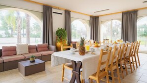 A dining area with a long table, chairs, and a sofa. There is a plant on the table and a window with curtains. - Beautiful private villa for 12 guests with WIFI, private pool, A/C and TV, close to Ostuni (San Vito Dei Normanni)