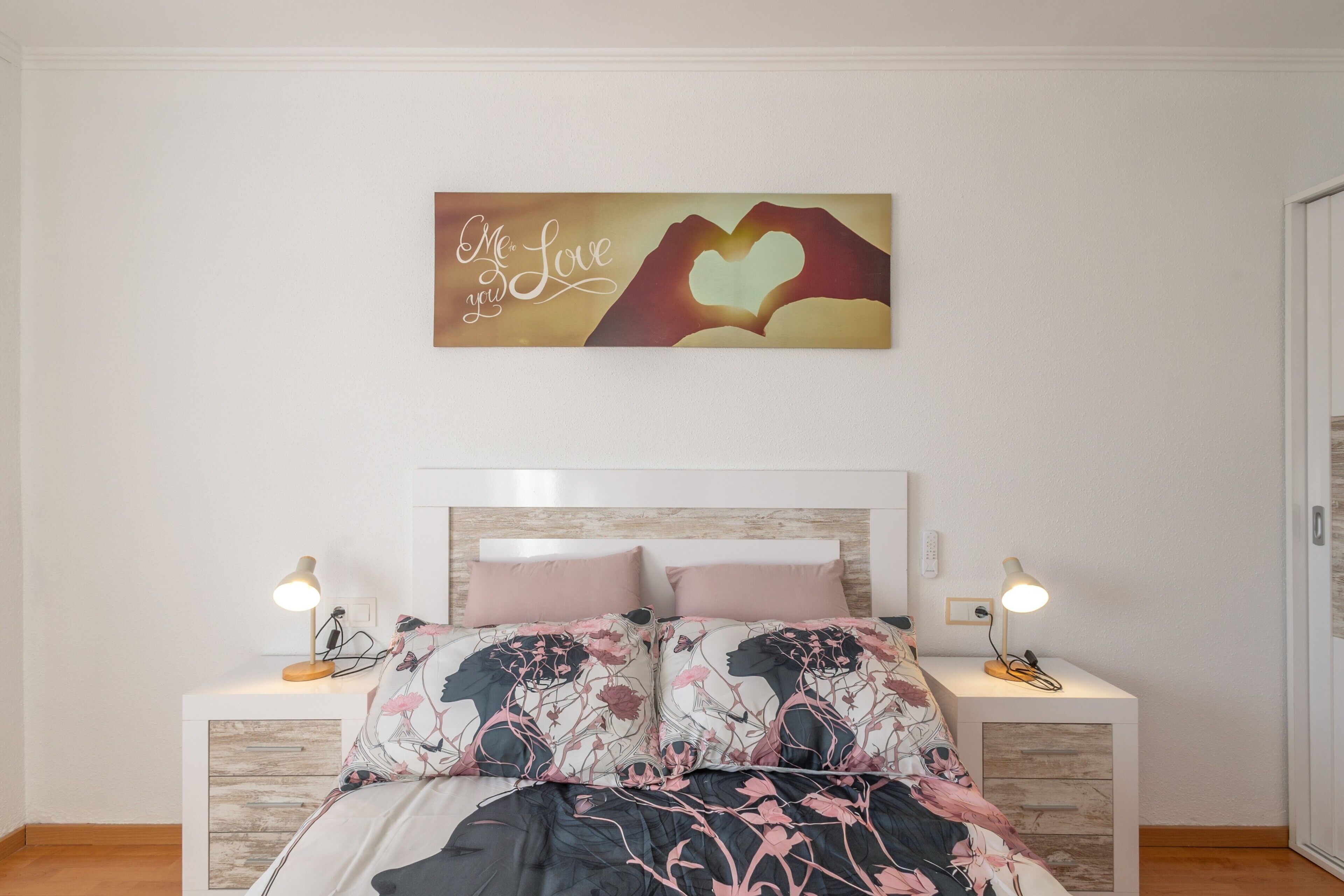 A bedroom with a bed, two bedside tables, a nightstand, a wall-mounted artwork, and a headboard.