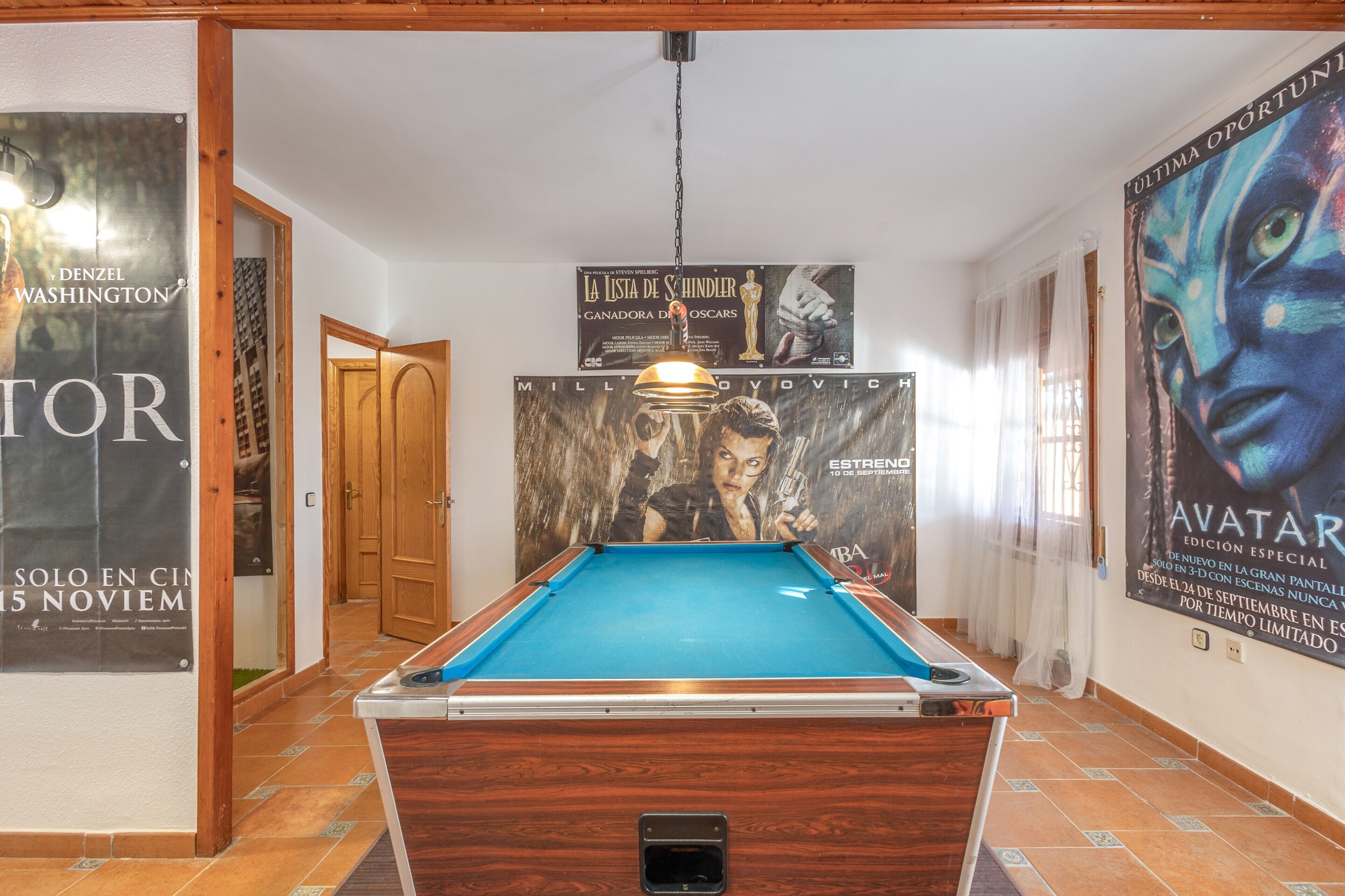 Una mesa de billar en una habitación con suelo de madera, carteles en las paredes y una puerta que da a otra estancia.