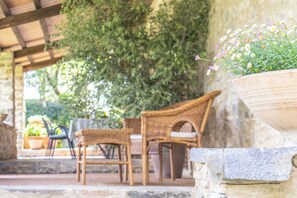 Mobili in vimini, un vaso in pietra con fiori e un muro in pietra.
