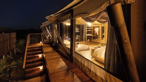 Un alloggio in tenda con un patio in legno, un letto con biancheria da letto bianca e una finestra con tende.