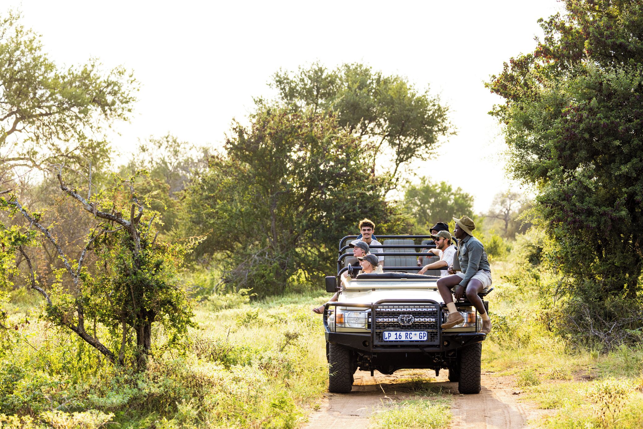 A vehicle with four passengers on a dirt road surrounded by trees.