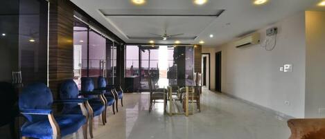 A spacious room with a modern ceiling design, a glass partition, and a seating area with blue chairs.