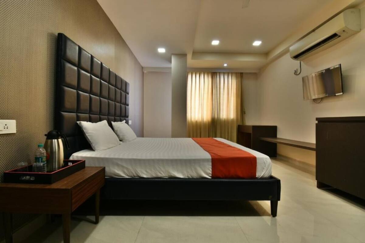 A modern hotel room with a large bed, a bedside table, a TV, and an air conditioning unit.