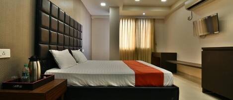 A modern hotel room with a large bed, a bedside table, a TV, and an air conditioning unit.