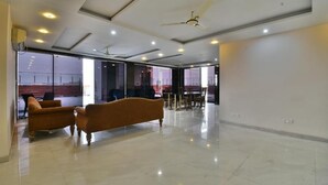 A spacious, well-lit room with a large sofa, ceiling fans, and a view through large windows. - THE CLOVERS INN (Patna)