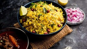 A bowl of yellow rice garnished with herbs and pomegranate seeds, accompanied by a lemon wedge and chopped red onions. - THE CLOVERS INN (Patna)