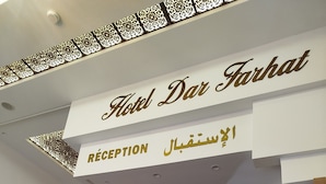 A hotel reception area with a sign reading "Hotel Dar Farhat" and "RECEPTION" in multiple languages. There are flags of various countries displayed, a wooden reception desk, and a wall-mounted security camera. - Hotel dar farhat (Tunis)