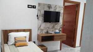A bedroom with a bed, a TV mounted on a marble wall, a wooden nightstand, and a wooden door. - Hotel dar farhat (Tunis)
