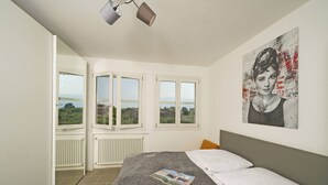 Een slaapkamer met een bed, een raam, een radiator en een schilderij aan de muur.