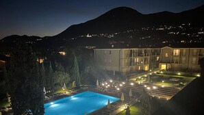 Een nachtzicht van een hotel met een zwembad, terras en een bergachtig landschap.