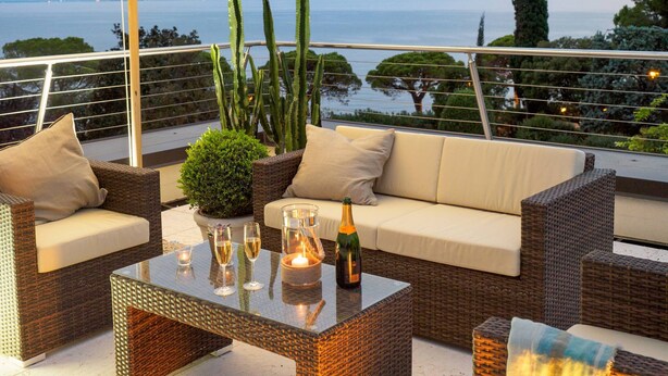 Een balkon met rieten meubels, een glazen tafel en uitzicht op zee.