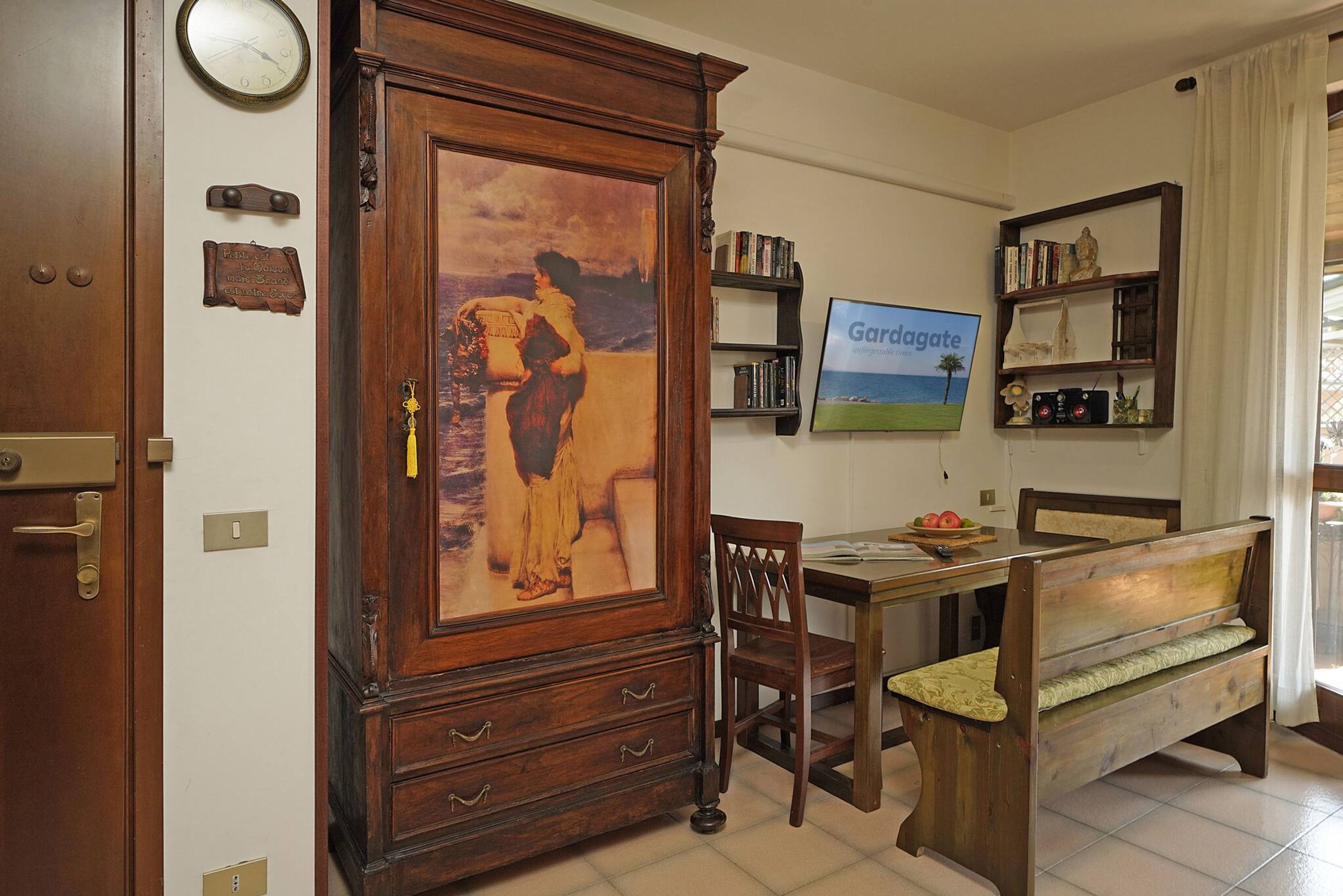 A room with a wooden cabinet, a clock, a framed picture, a bookshelf, and a bench.