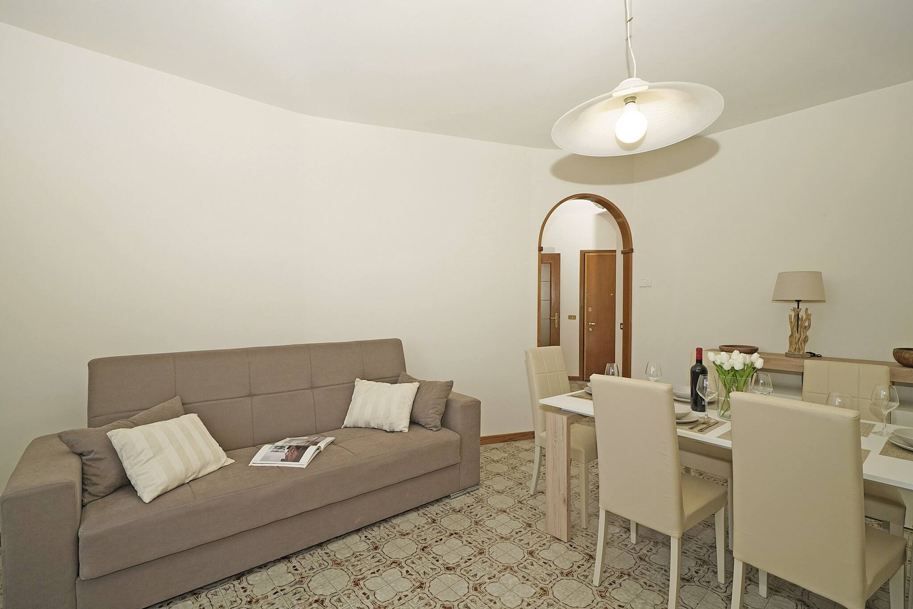 A modern living room with a sofa, dining table, chairs, and a hanging light fixture.