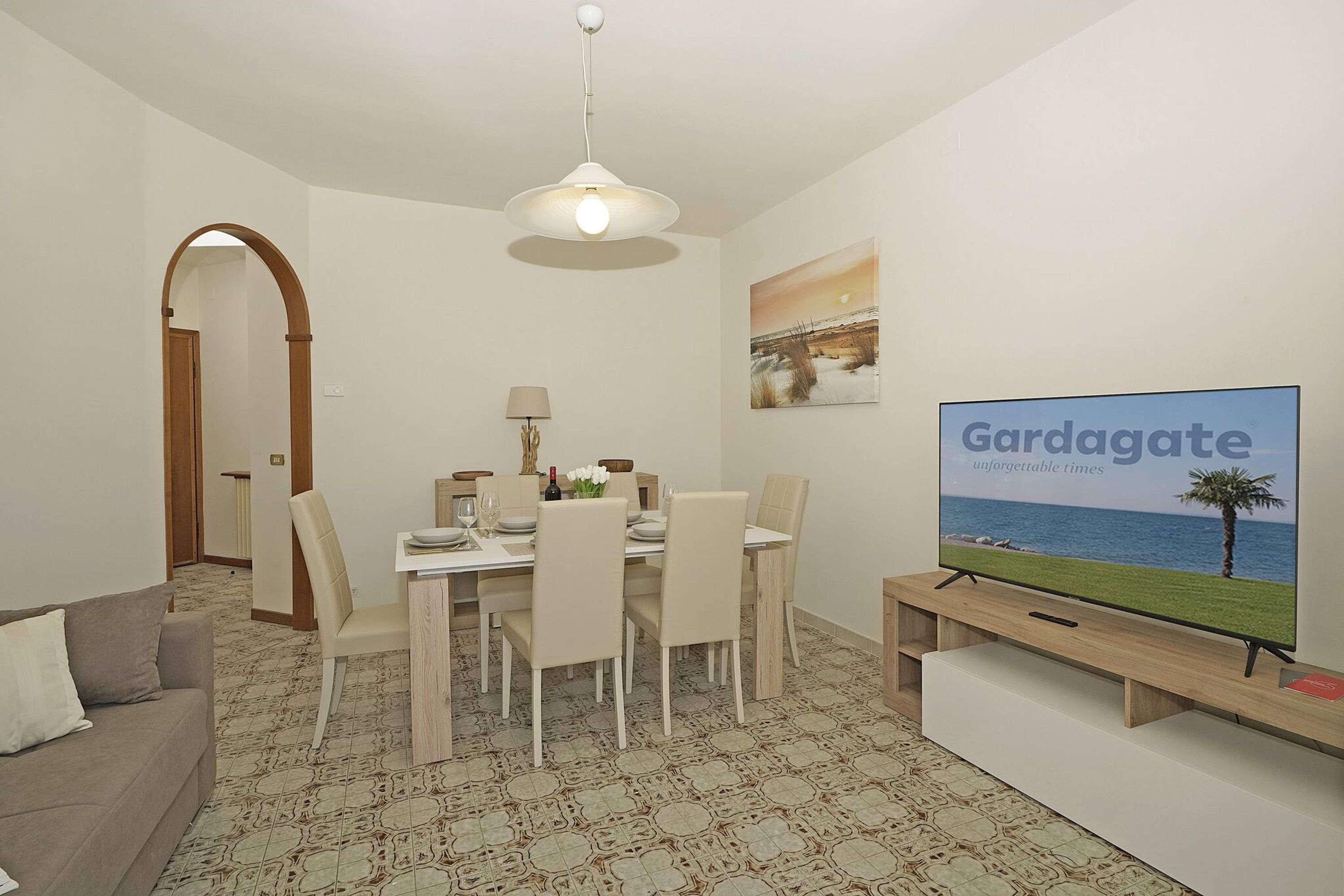 A dining area with a table set for four, a television on a stand, and a painting on the wall.