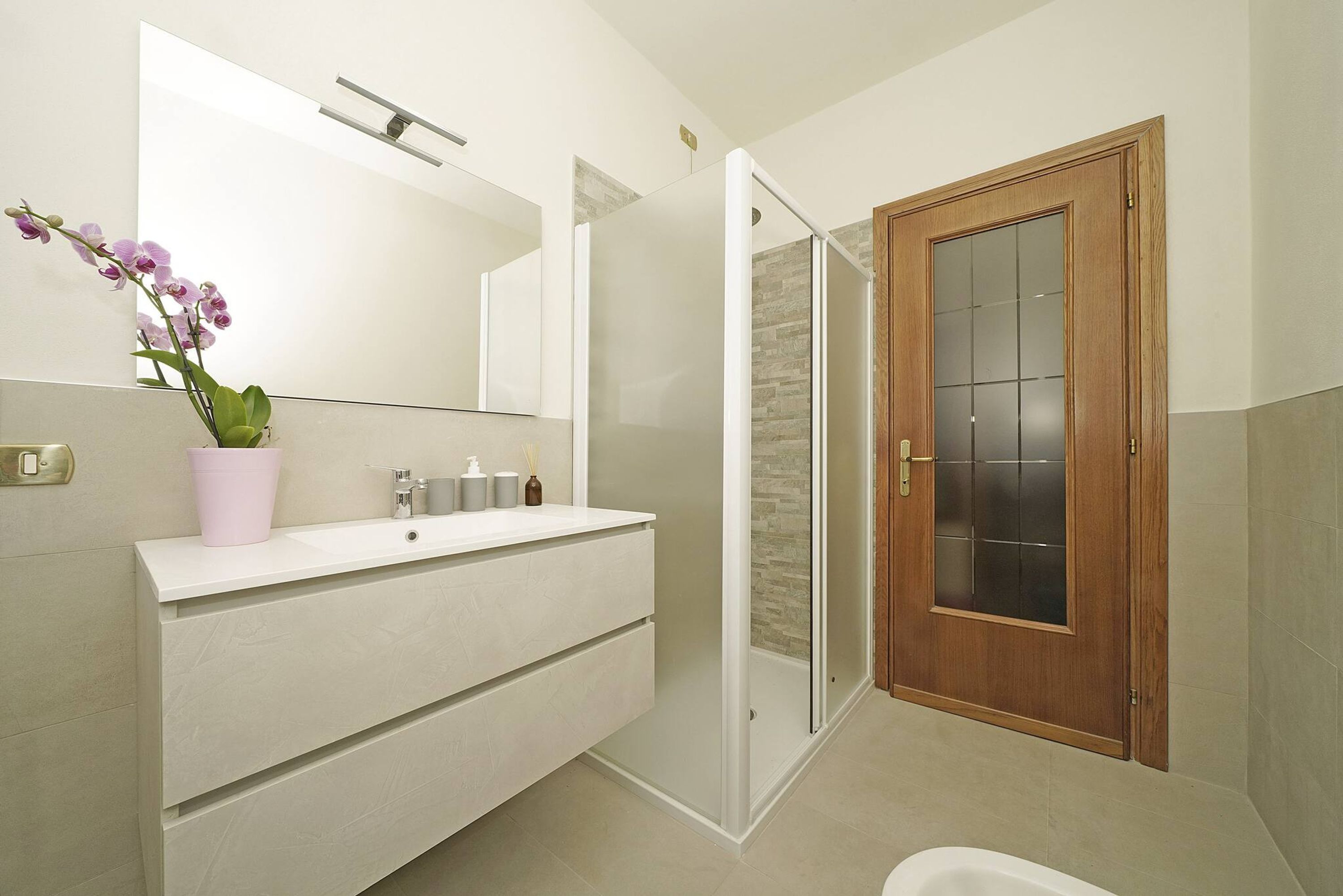 A modern bathroom with a white vanity, a glass shower enclosure, and a wooden door.
