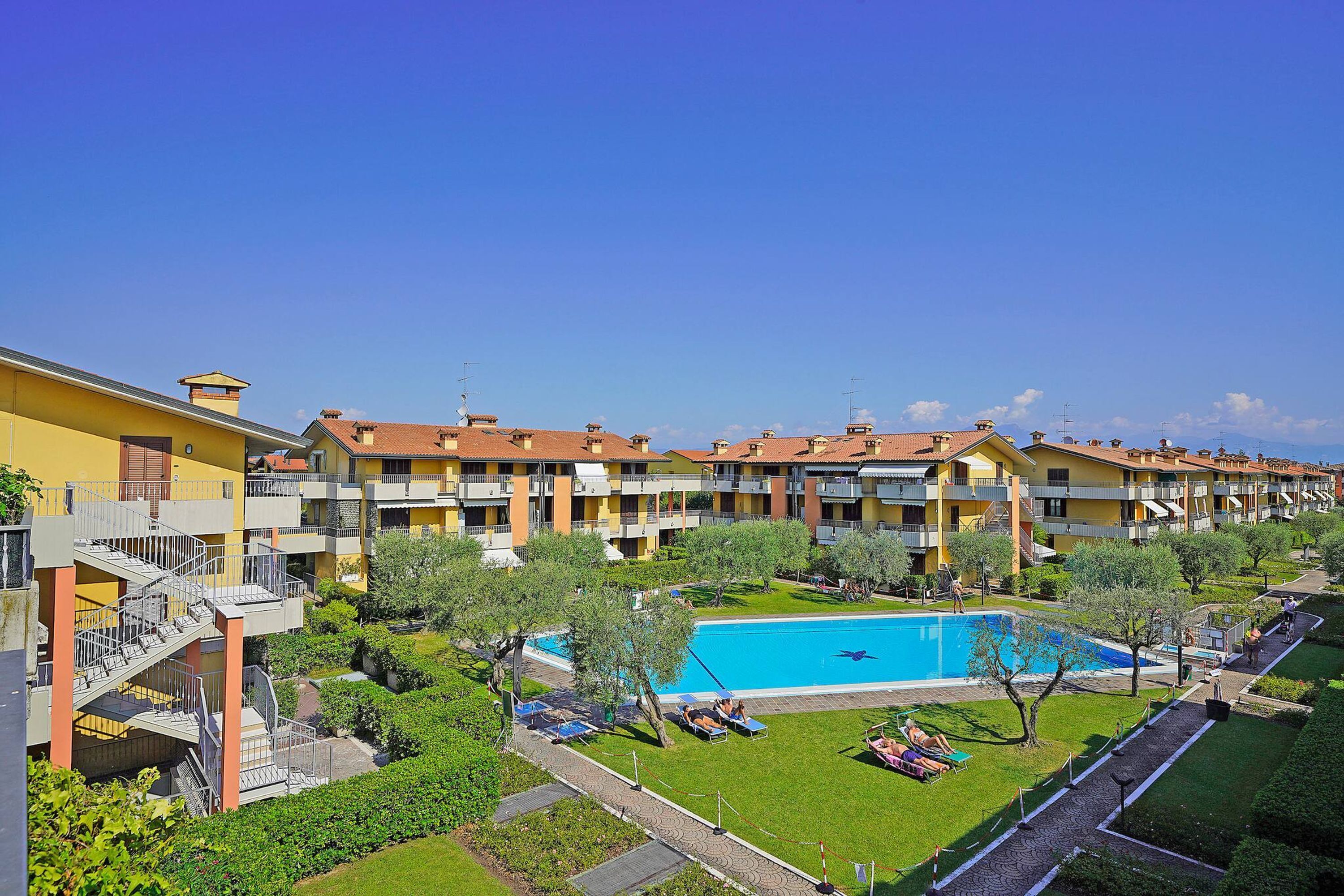 A hotel with multiple balconies, a swimming pool, and well-maintained gardens.