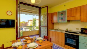 A compact kitchen with wooden cabinets, a built-in oven, and a dining area with a table set for breakfast. - Villaggio dei Fiori - Viola (Sirmione)