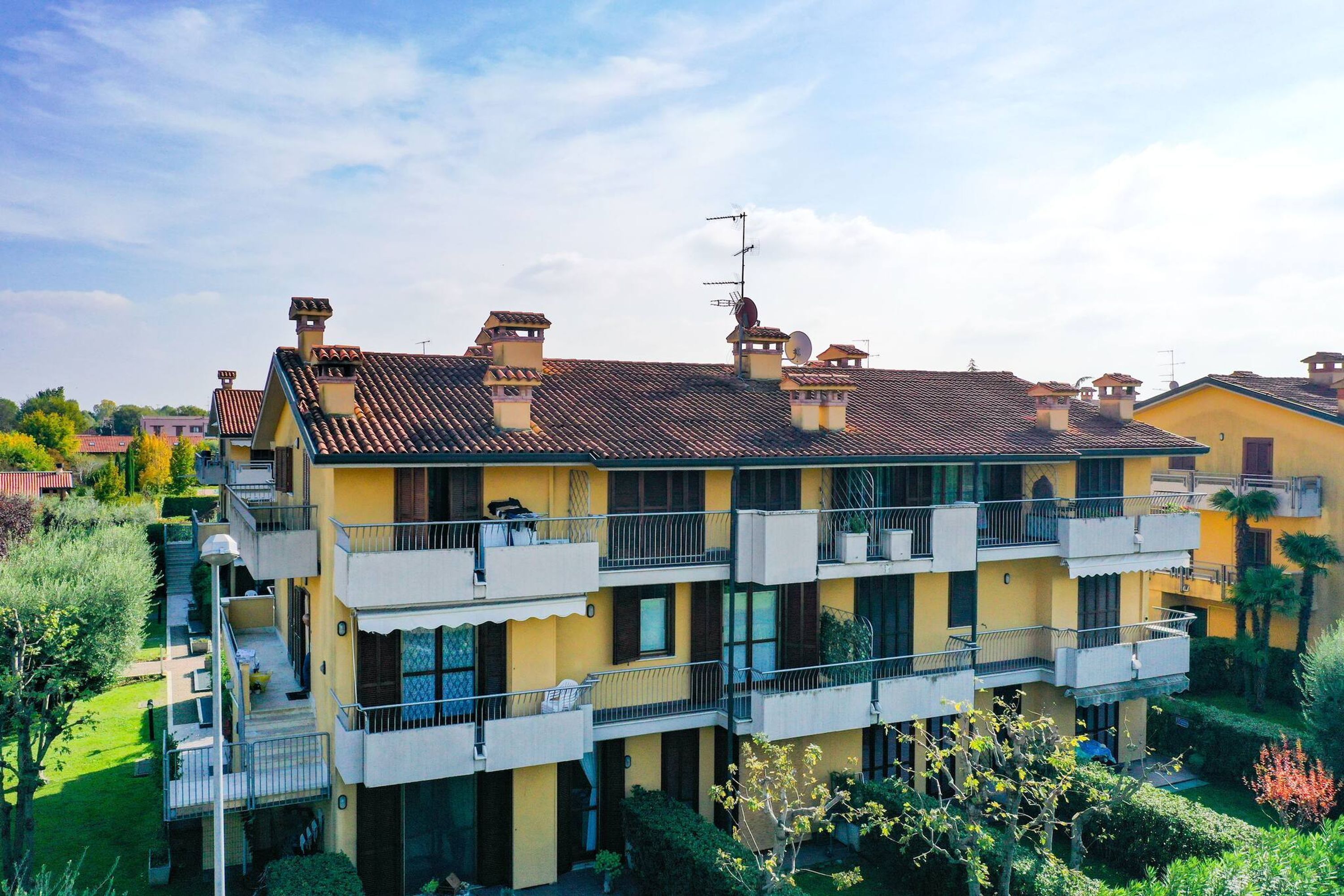 Un edificio de varios pisos con balcones, techo de tejas y un jardín.