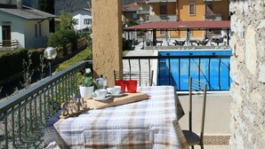 A balcony with a table set for dining, overlooking a swimming pool and a mountainous landscape. - Casa Anna 701 in Gardola (Tignale)