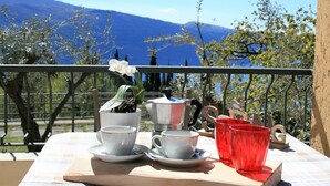 A table with cups and a red glass on a balcony with a mountain view. - Casa Anna 701 in Gardola (Tignale)