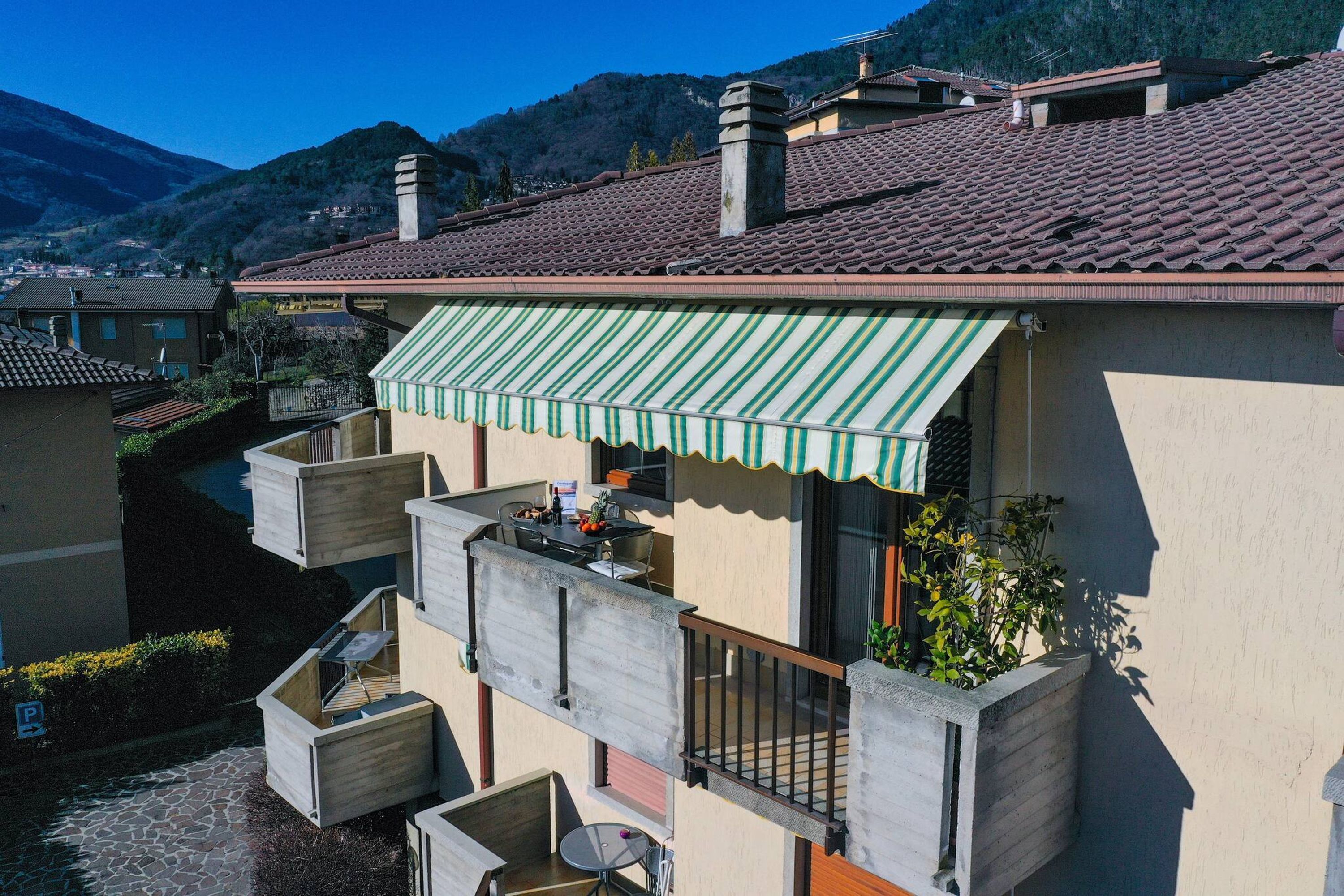 A residential building with a tiled roof, a balcony with a striped awning, and a stone-paved courtyard.
