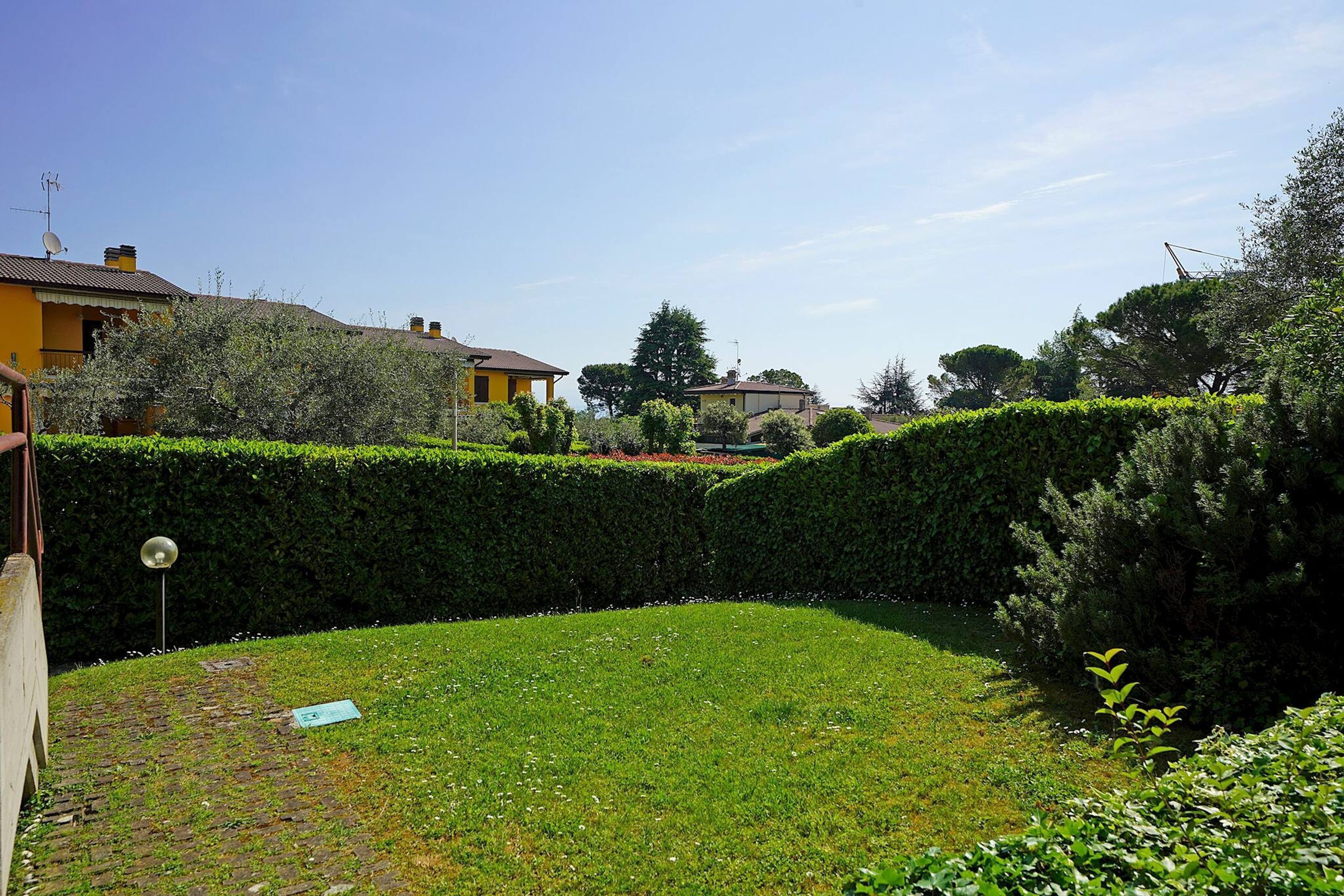 A residential garden with hedges, a brick pathway, and a satellite dish.