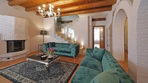 A spacious living room with a fireplace, a green sofa, a coffee table, and a chandelier. - Villa Cedro - Gardagate (Verona)