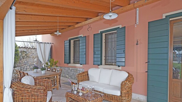 A covered outdoor seating area with wicker furniture, a white sofa, and a stone wall in the background. - Villa Cedro - Gardagate (Verona)