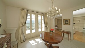 A dining area with a wooden table, a chandelier, and a view of the outdoors through large windows. - Villa San Carlo - Gardagate (Roe Volciano)