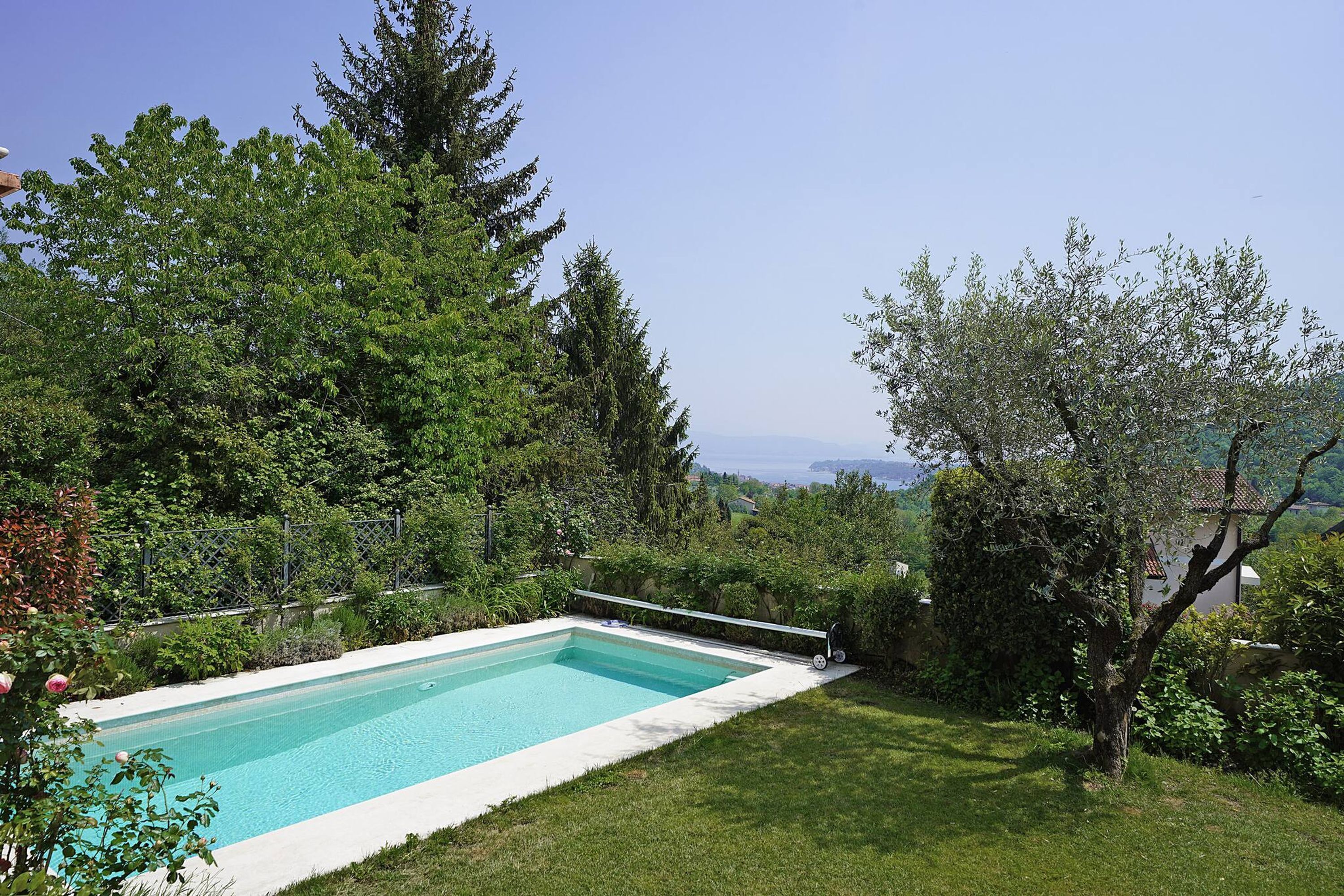 A rectangular swimming pool surrounded by lush greenery and trees, with a clear view of the landscape in the background.