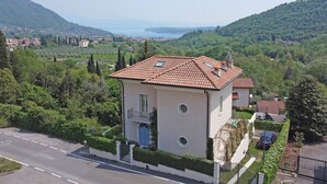 A two-story building with a tiled roof, a balcony, and a circular window. - Villa San Carlo - Gardagate (Roe Volciano)