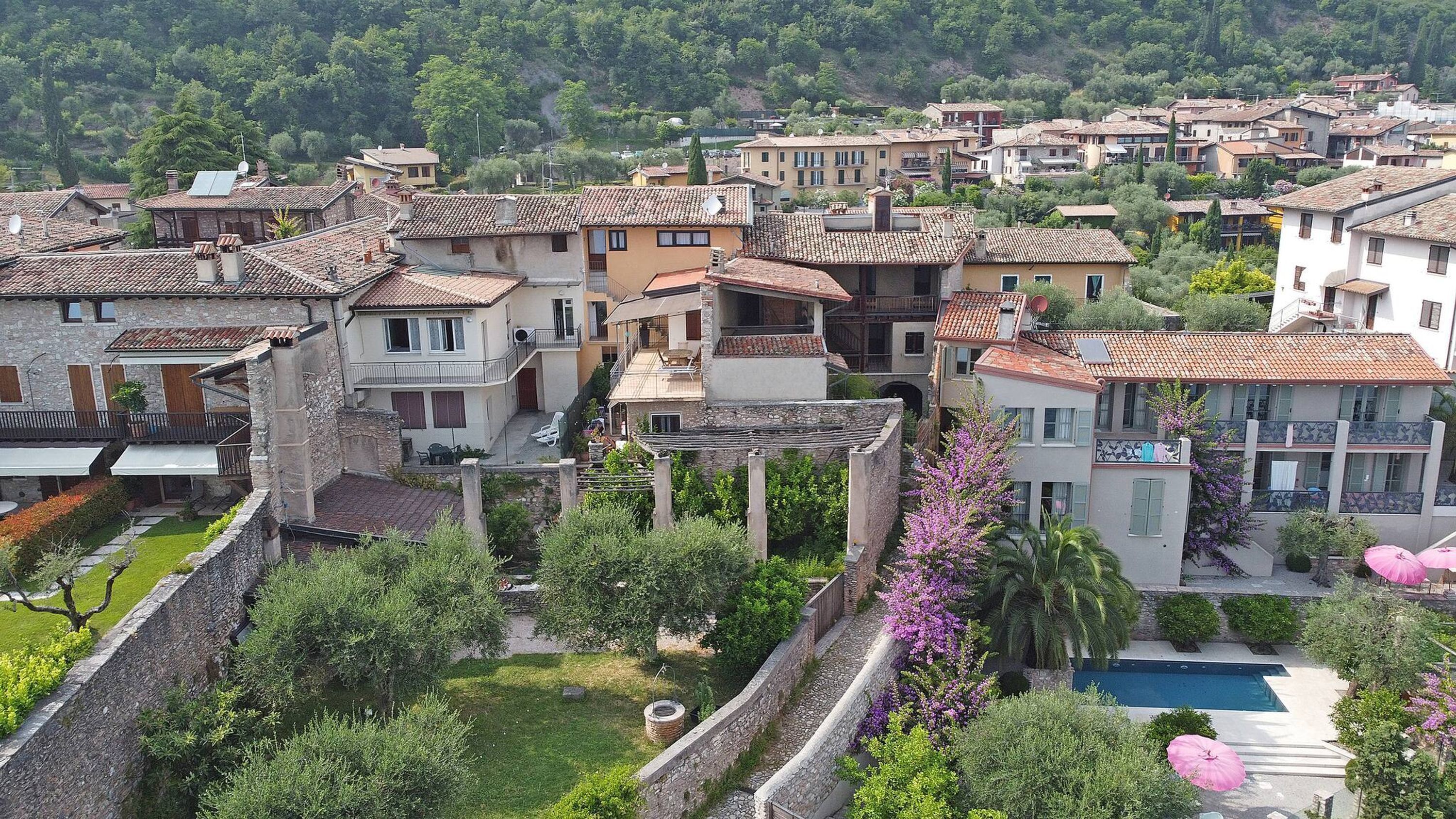 A residential area with terracotta-tiled roofs, stone walls, and lush greenery.