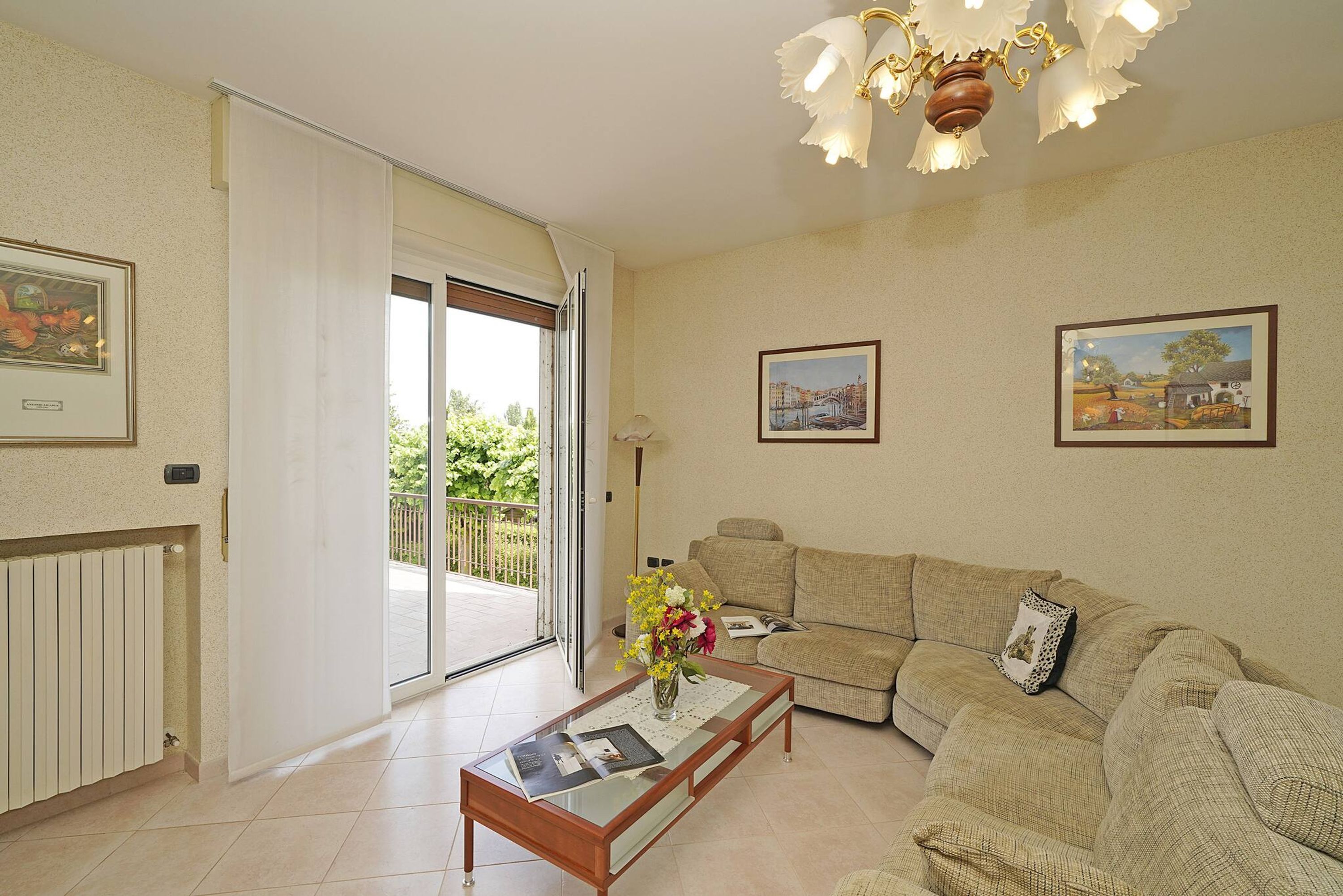 Ein Wohnzimmer mit einer Couch, einem Couchtisch mit Blumenvase und einer Glastür zum Balkon.