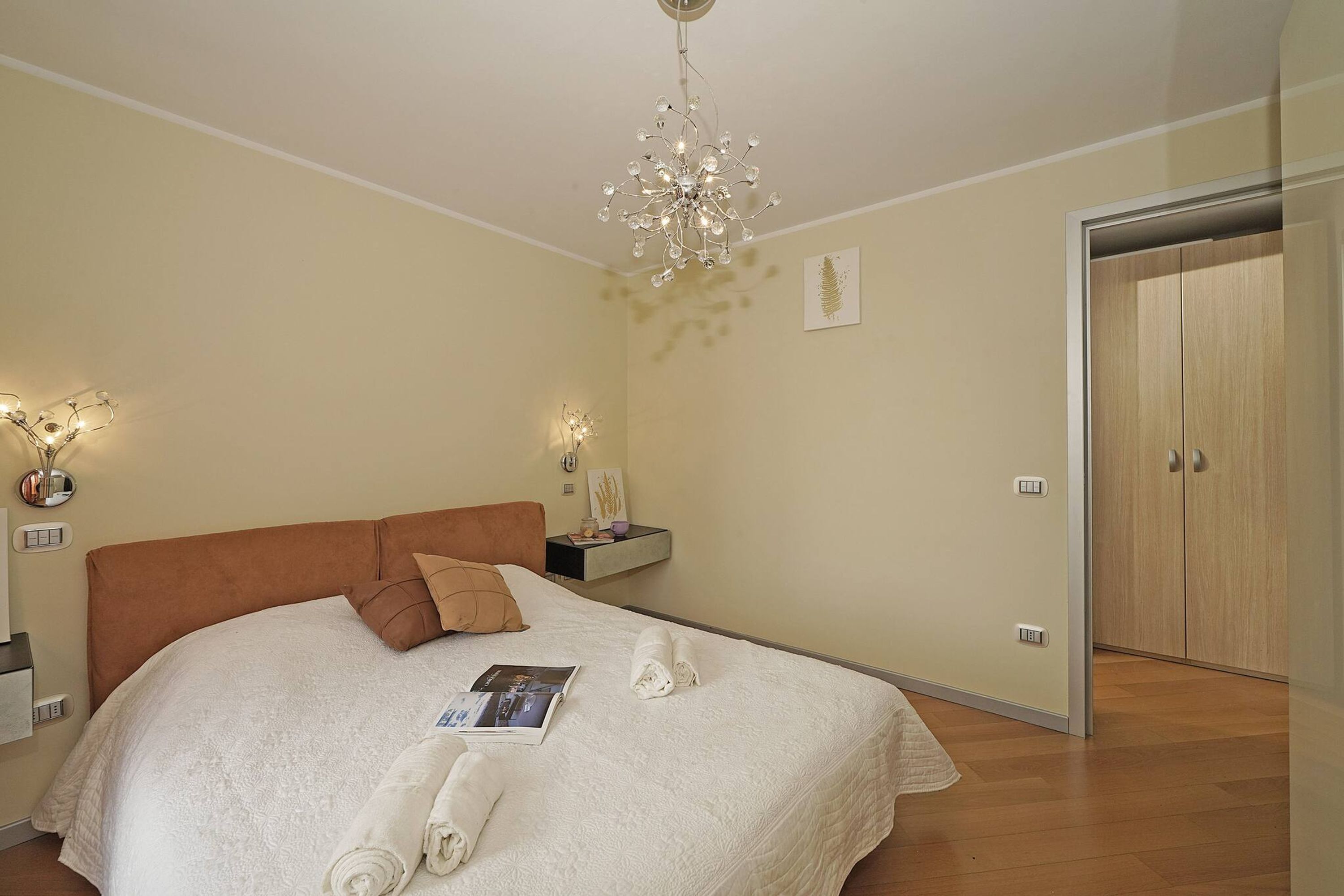 Una cama bien hecha con cabecera marrón, una mesita de noche con lámpara y un armario de madera.