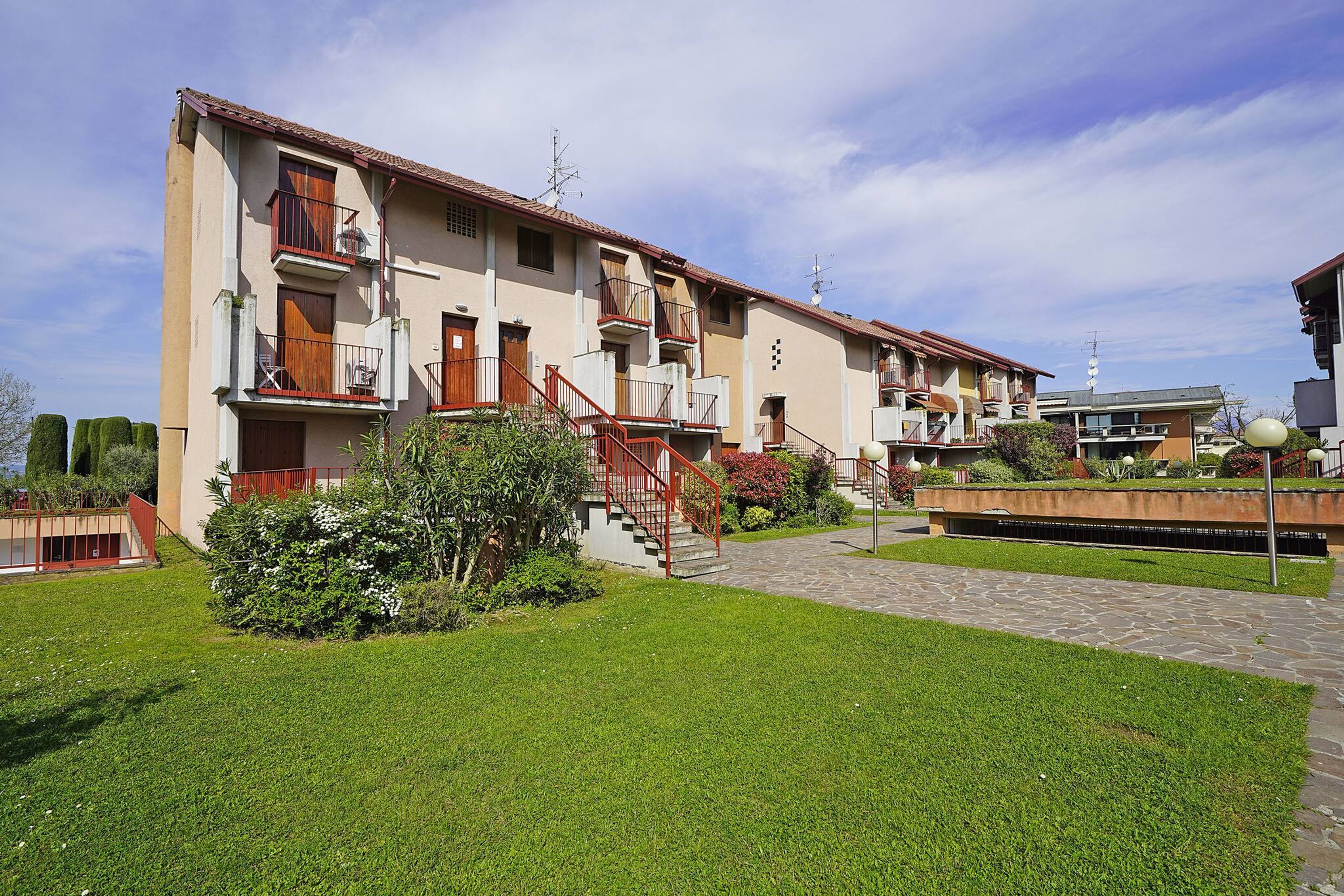 Un edificio residencial de varios pisos con balcones, un camino de piedra y abundante vegetación.
