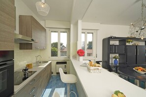 Een moderne keuken met een vaatwasser, een spoelbak en een kookplaat. Twee ramen zorgen voor natuurlijk licht, en er is een eethoek met een tafel en stoelen.