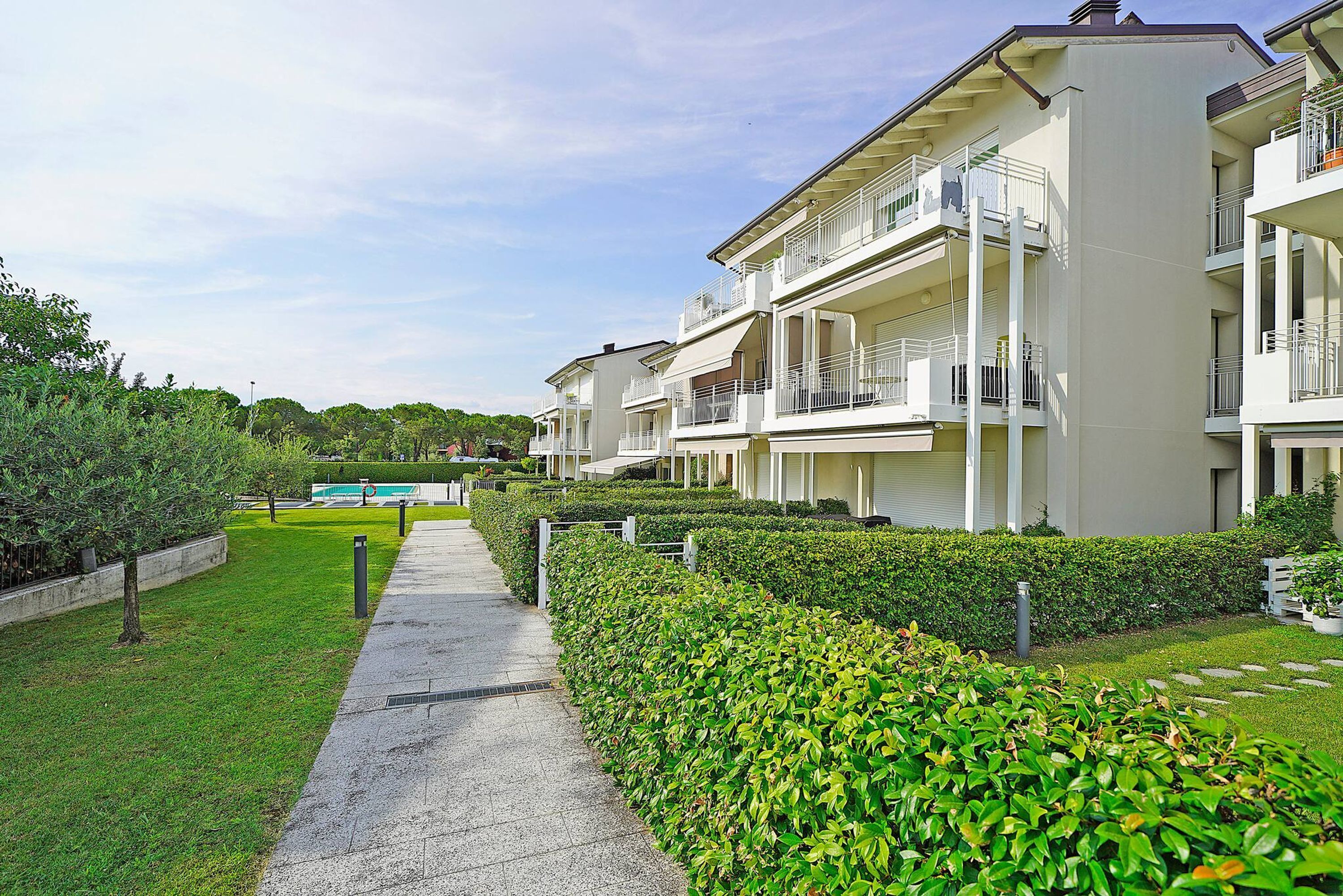 A row of modern apartment buildings with balconies, a paved walkway, and well-maintained greenery.