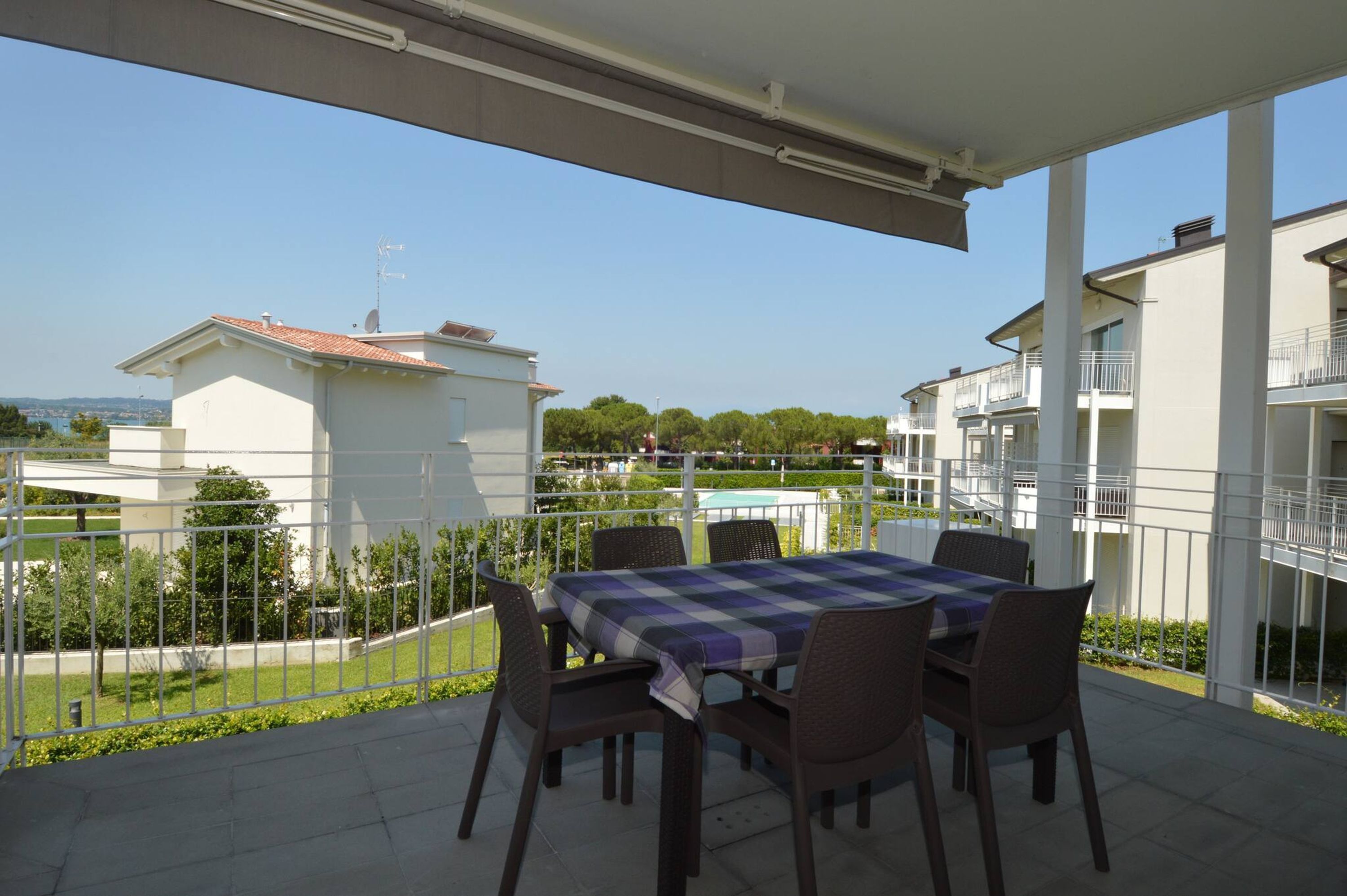 A covered outdoor dining area with a table and chairs, a view of neighboring buildings, and a clear sky.