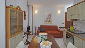 A compact living space with a dining table, sofa, kitchenette, and a cabinet with glass doors. - Casa Annalisa in Sal (Salò)