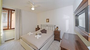 A bedroom with a bed, bedside tables, a ceiling fan, a window, and a radiator. - Casa Annalisa in Sal (Salò)