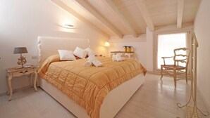 Um quarto com uma cama grande, uma mesa de cabeceira com abajur, uma cadeira e uma janela com cortinas.