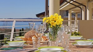Mesa posta para refeição com vista para o mar, um vaso de flores amarelas e um prato de pão.