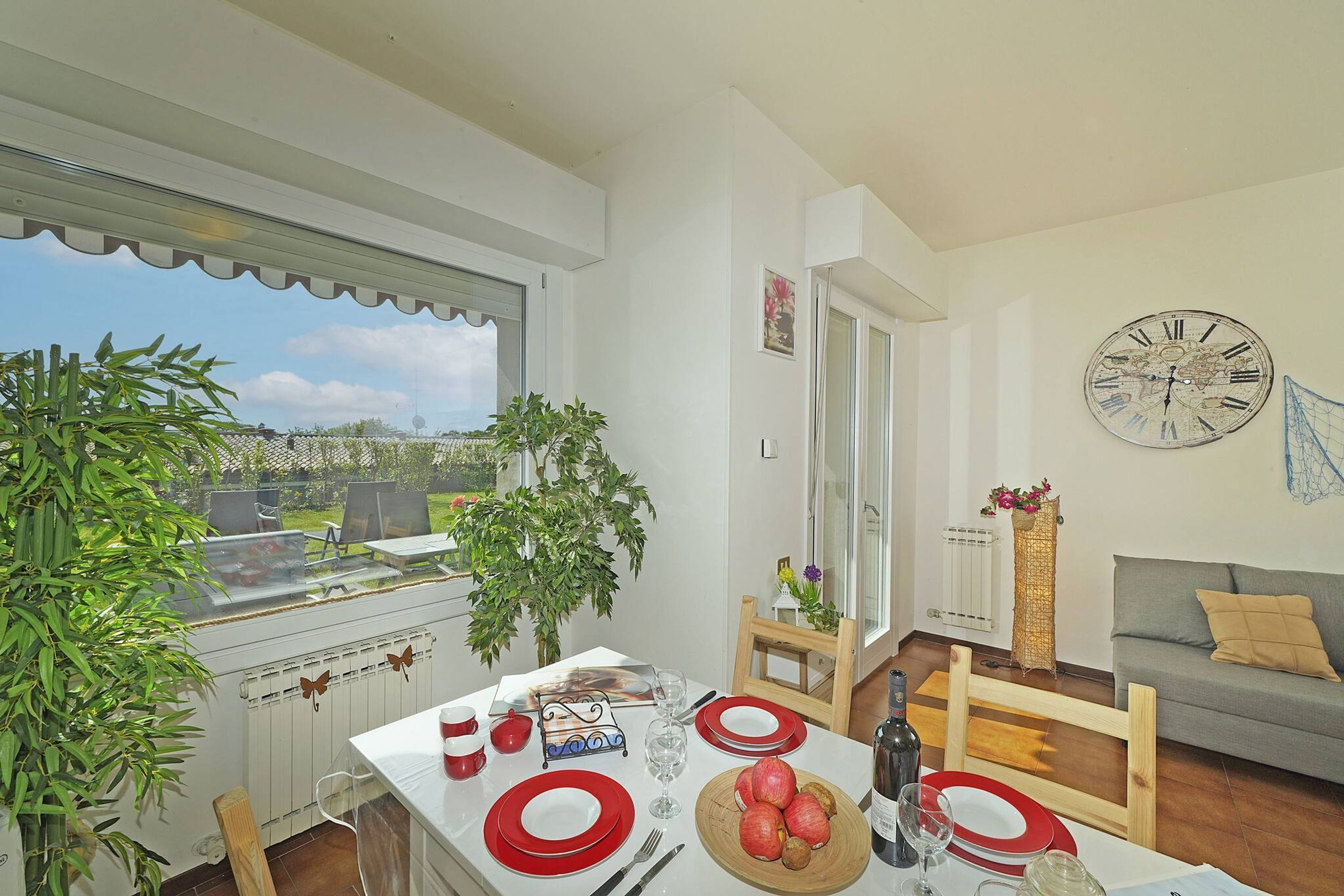 A dining area with a table set for two, a clock on the wall, and a view of the outdoors.