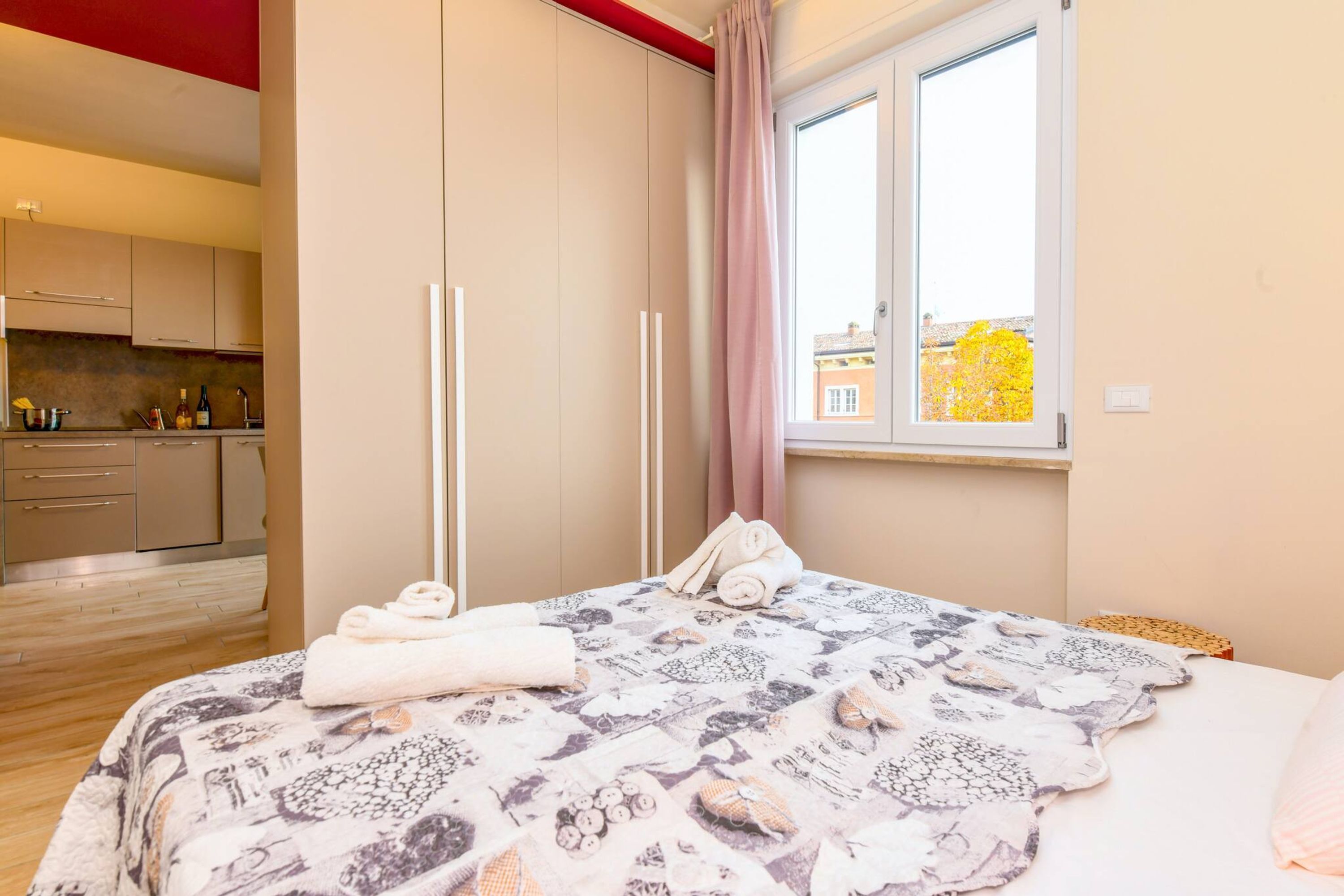 A bedroom with a bed, a window with a view, and a kitchen area.